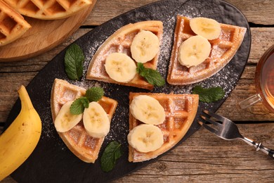 Tasty Belgian waffles with banana, mint and fork on wooden table, flat lay