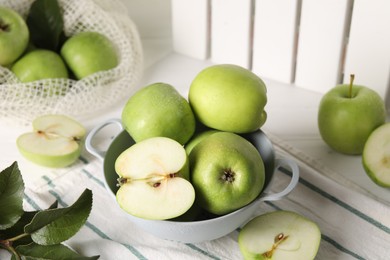 Fresh green apples with water drops and leaves on white table