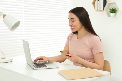 Home workplace. Happy woman with smartphone working on laptop at white desk in room