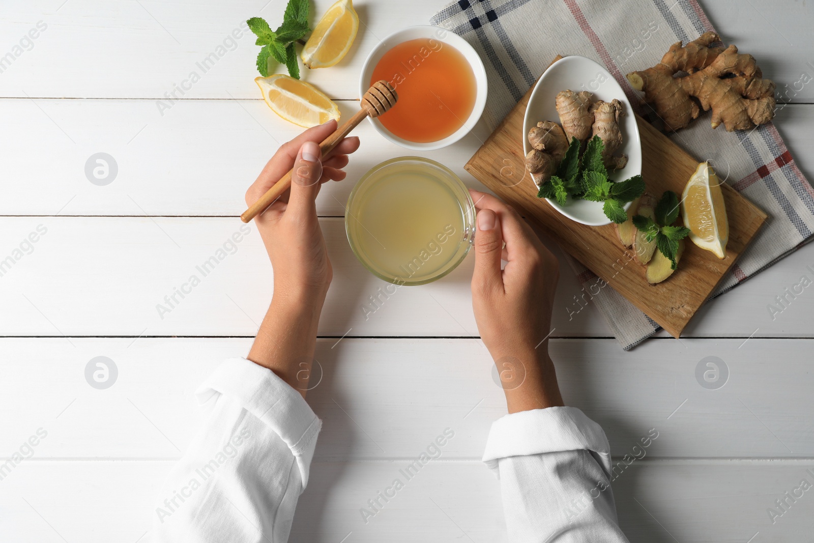 Photo of Woman drinking delicious ginger tea with honey at white wooden table, top view