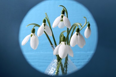 Beautiful snowdrops in vase against light blue background, view through paper frame
