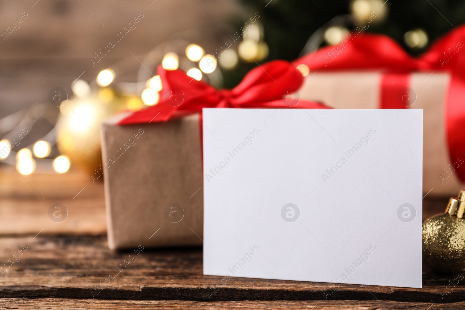 Photo of Blank Christmas card and golden bauble on wooden table, closeup. Space for text