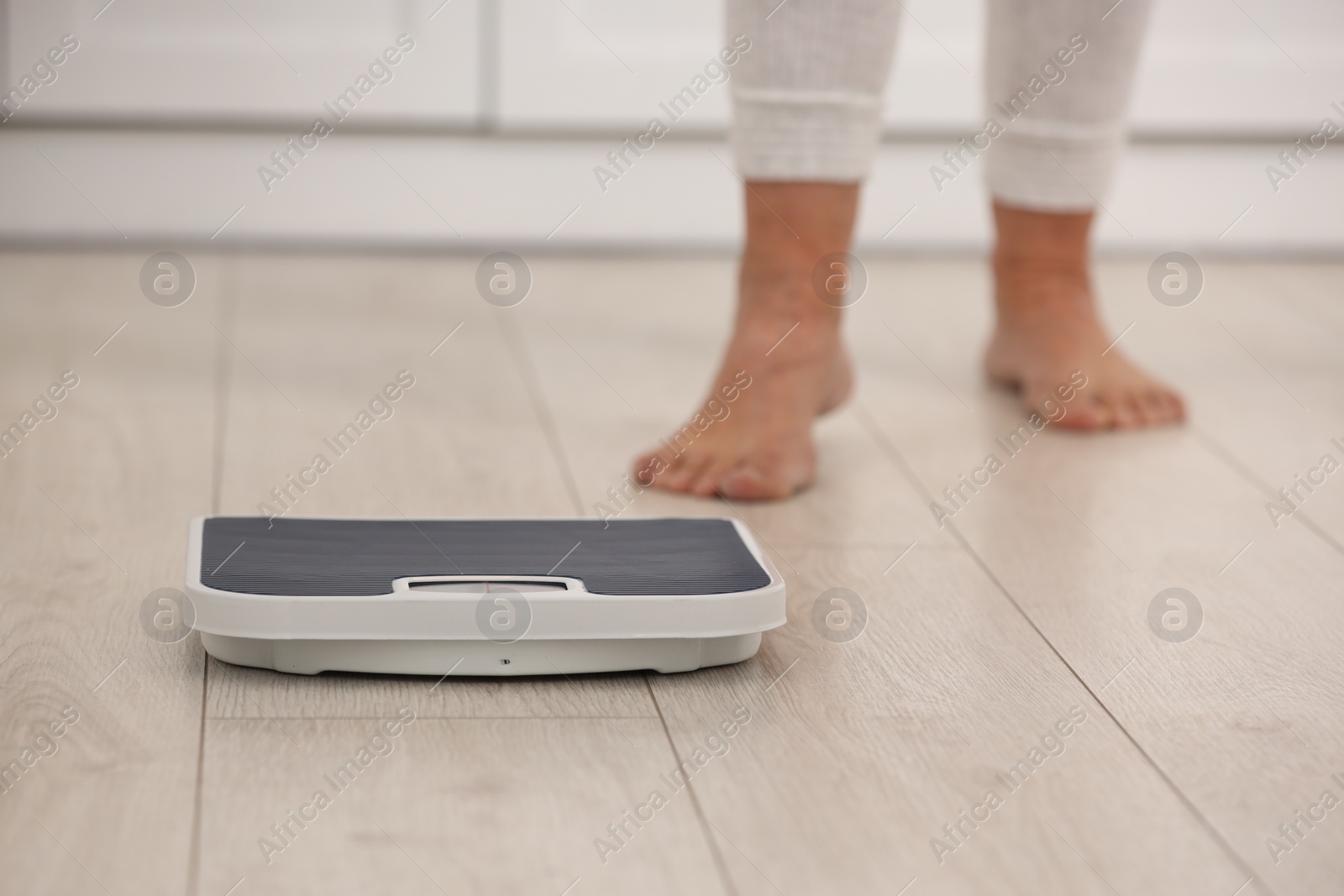 Photo of Menopause, weight gain. Woman standing on floor indoors, focus on scales