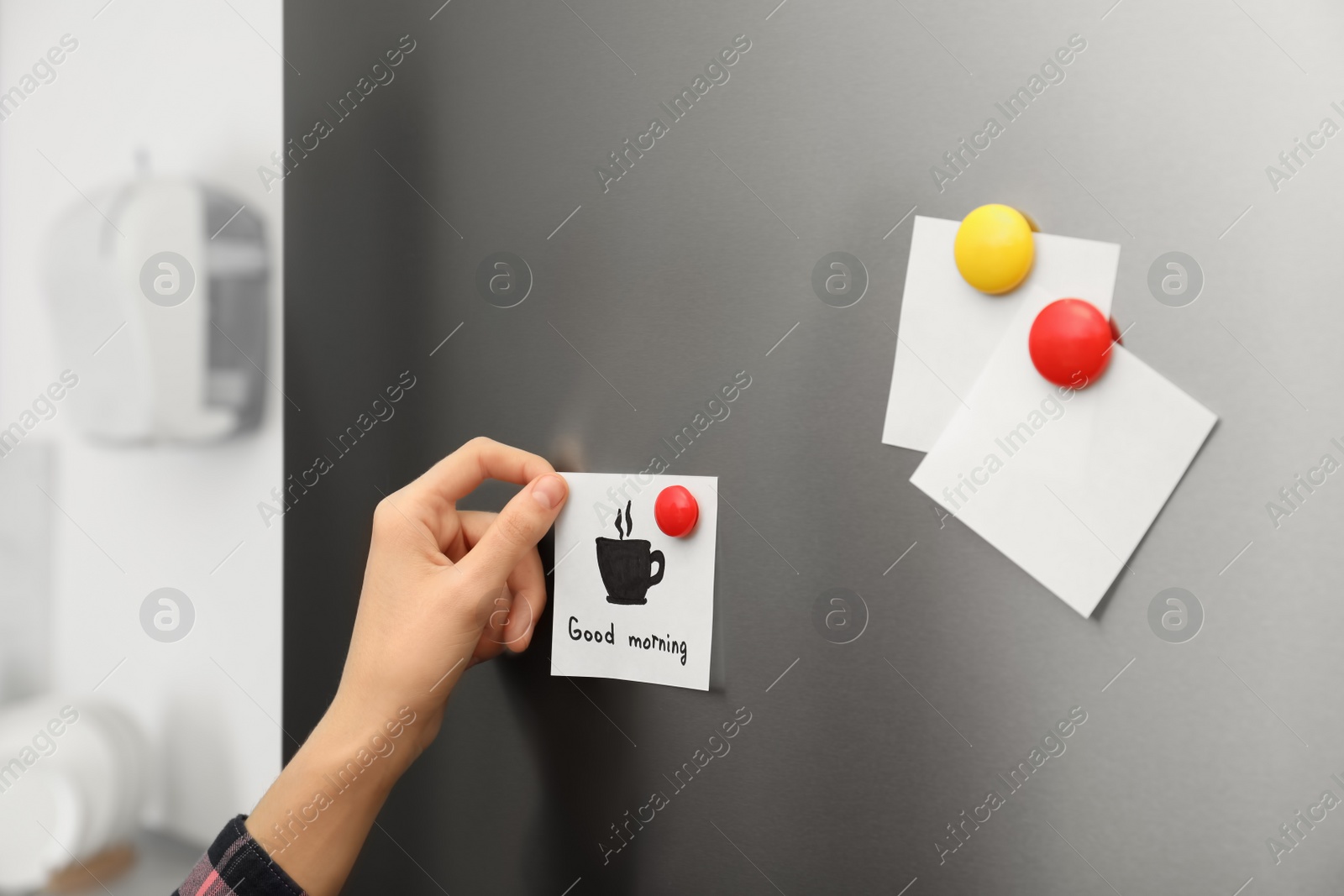 Photo of Woman putting paper sheet on refrigerator door at home, closeup