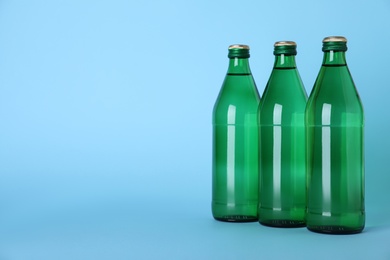 Photo of Glass bottles with water on light blue background, space for text