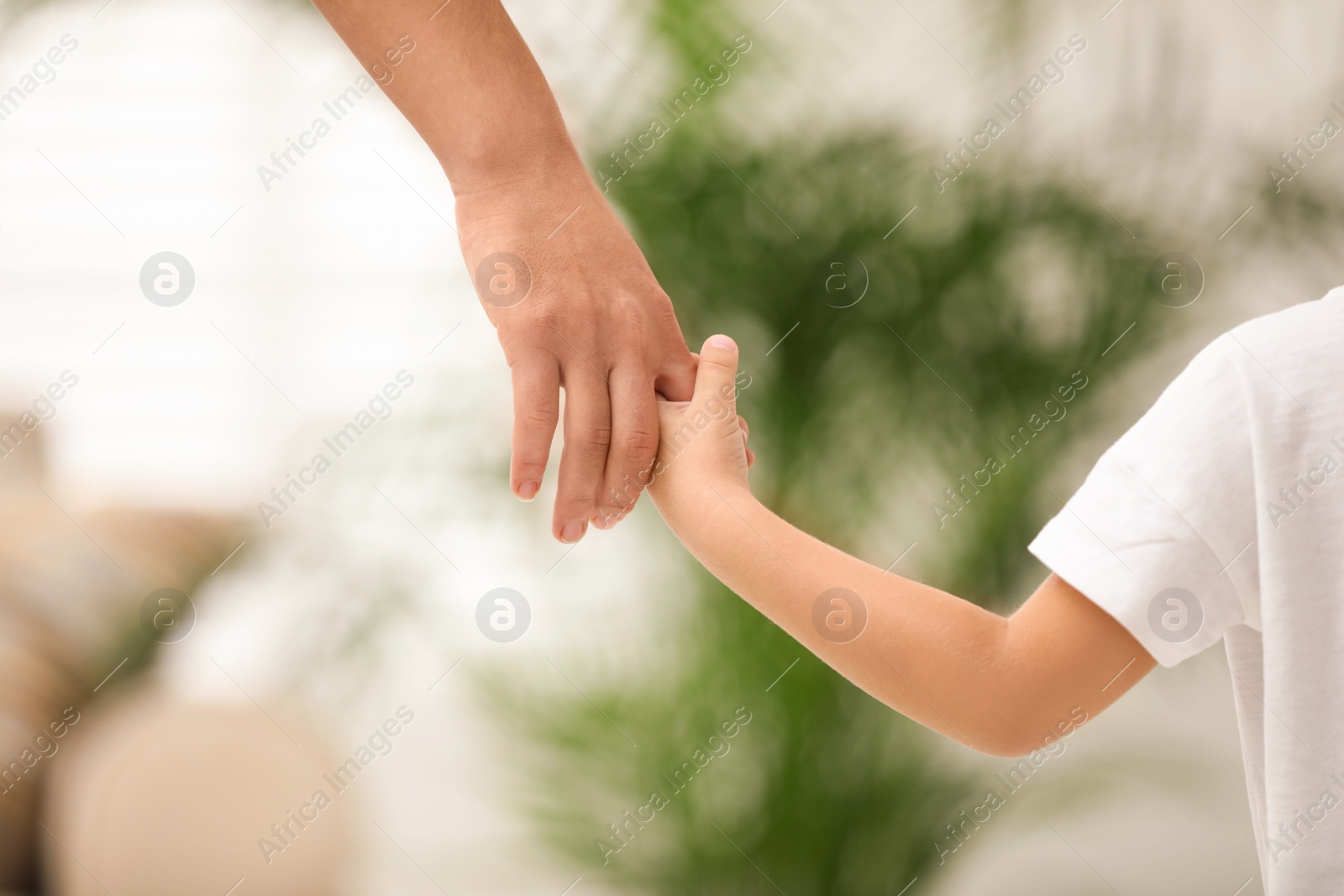 Photo of Mother holding hands with her child indoors, closeup. Happy family