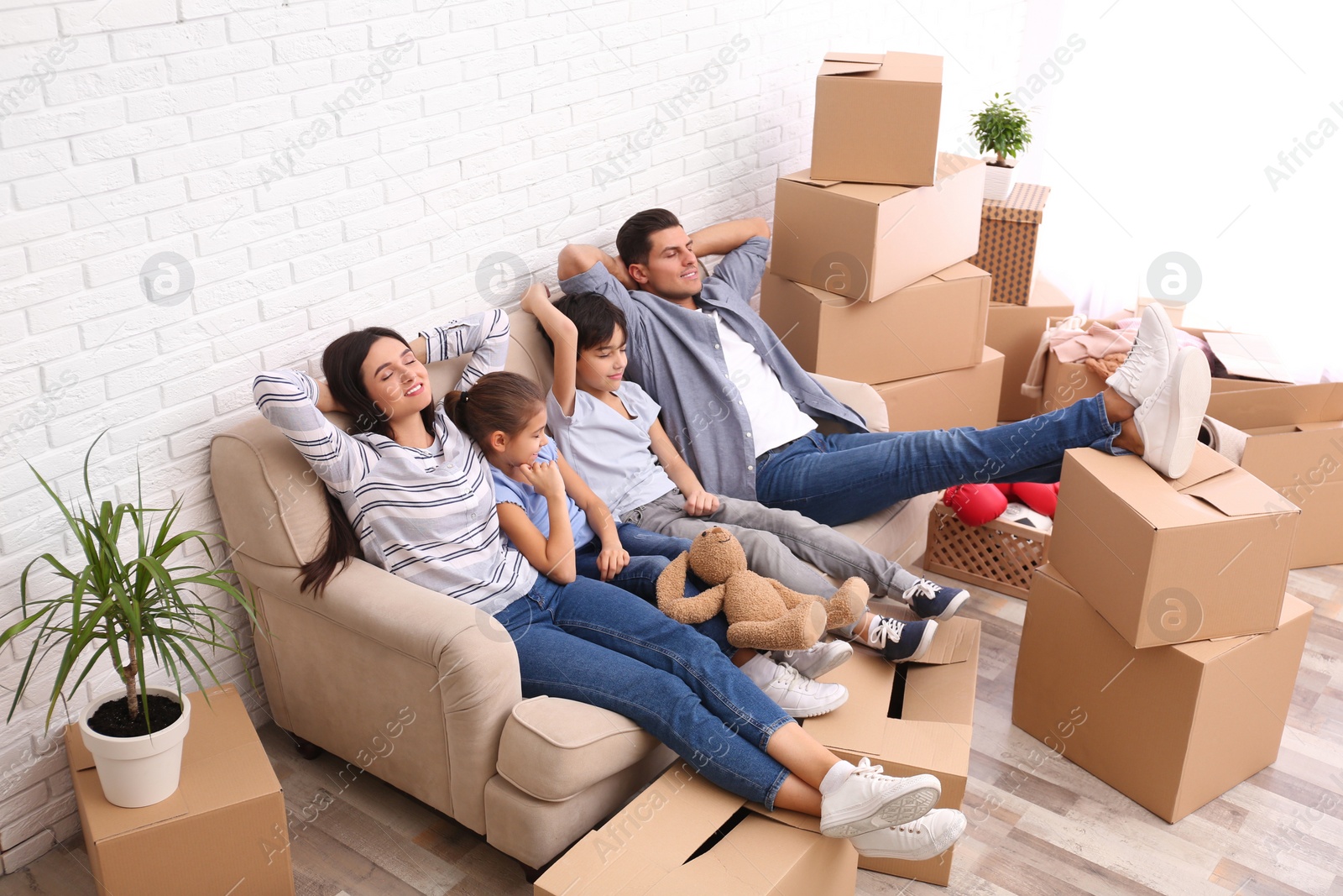 Photo of Happy family resting in room with cardboard boxes on moving day