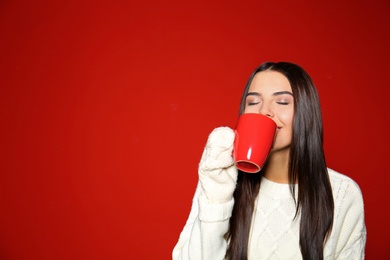 Young woman in warm sweater with cup of hot drink on red background. Space for text