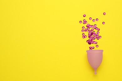 Menstrual cup with pink sequins on yellow background, flat lay. Space for text