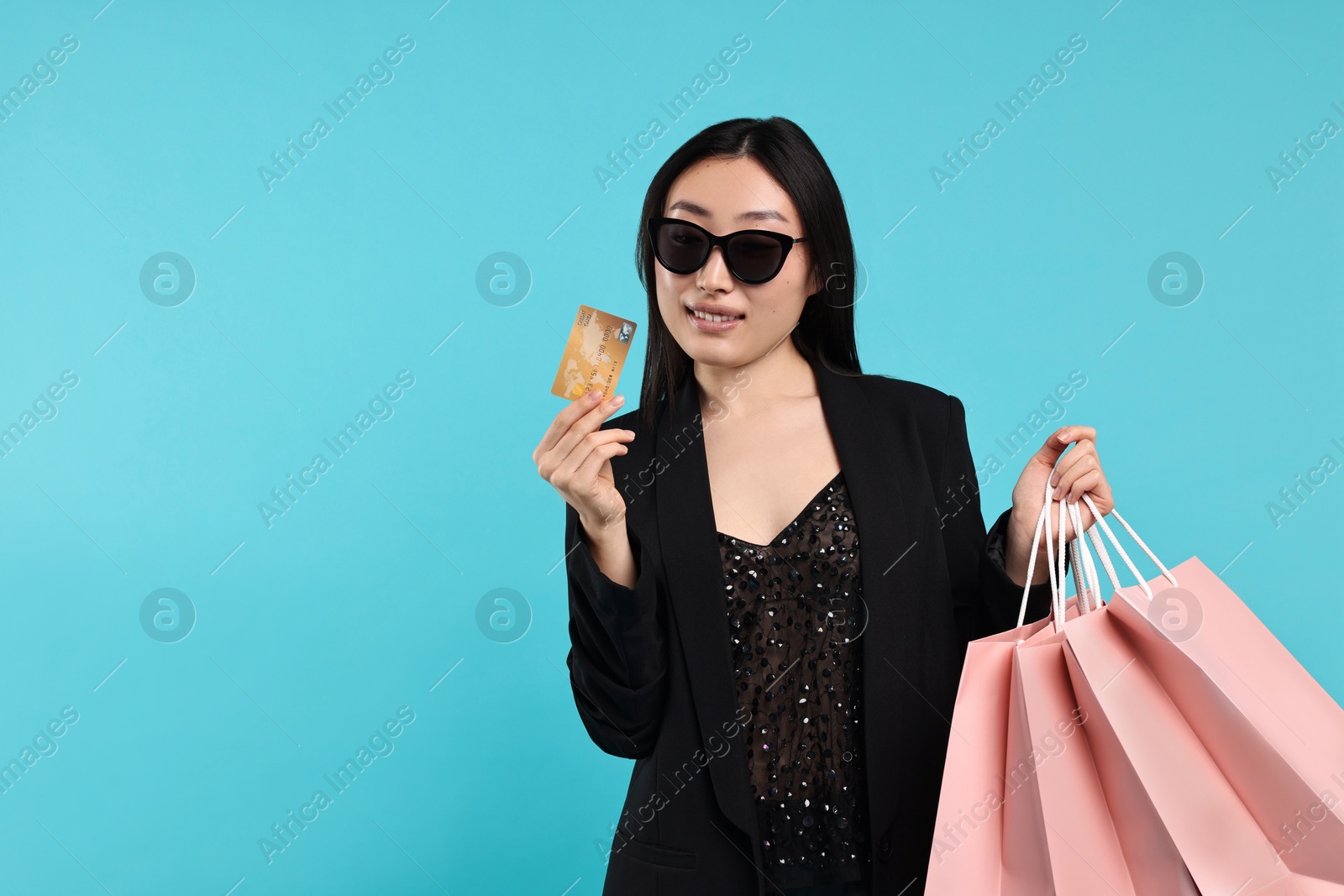 Photo of Smiling woman with shopping bags and credit card on light blue background. Space for text