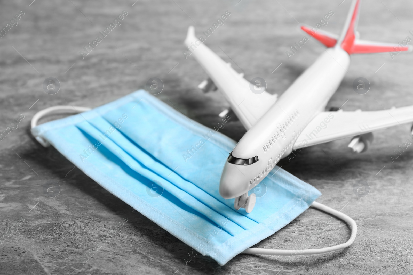 Photo of Toy airplane and medical mask on grey stone background, closeup. Travelling during coronavirus pandemic