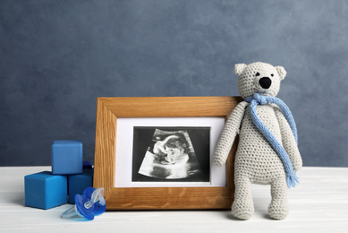 Photo of Composition with child's ultrasound photo and toys on white table