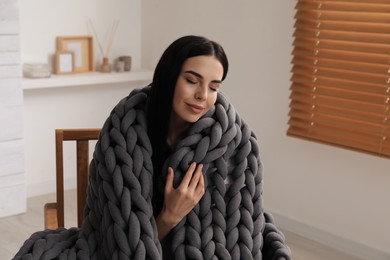 Photo of Young woman with chunky knit blanket in armchair at home