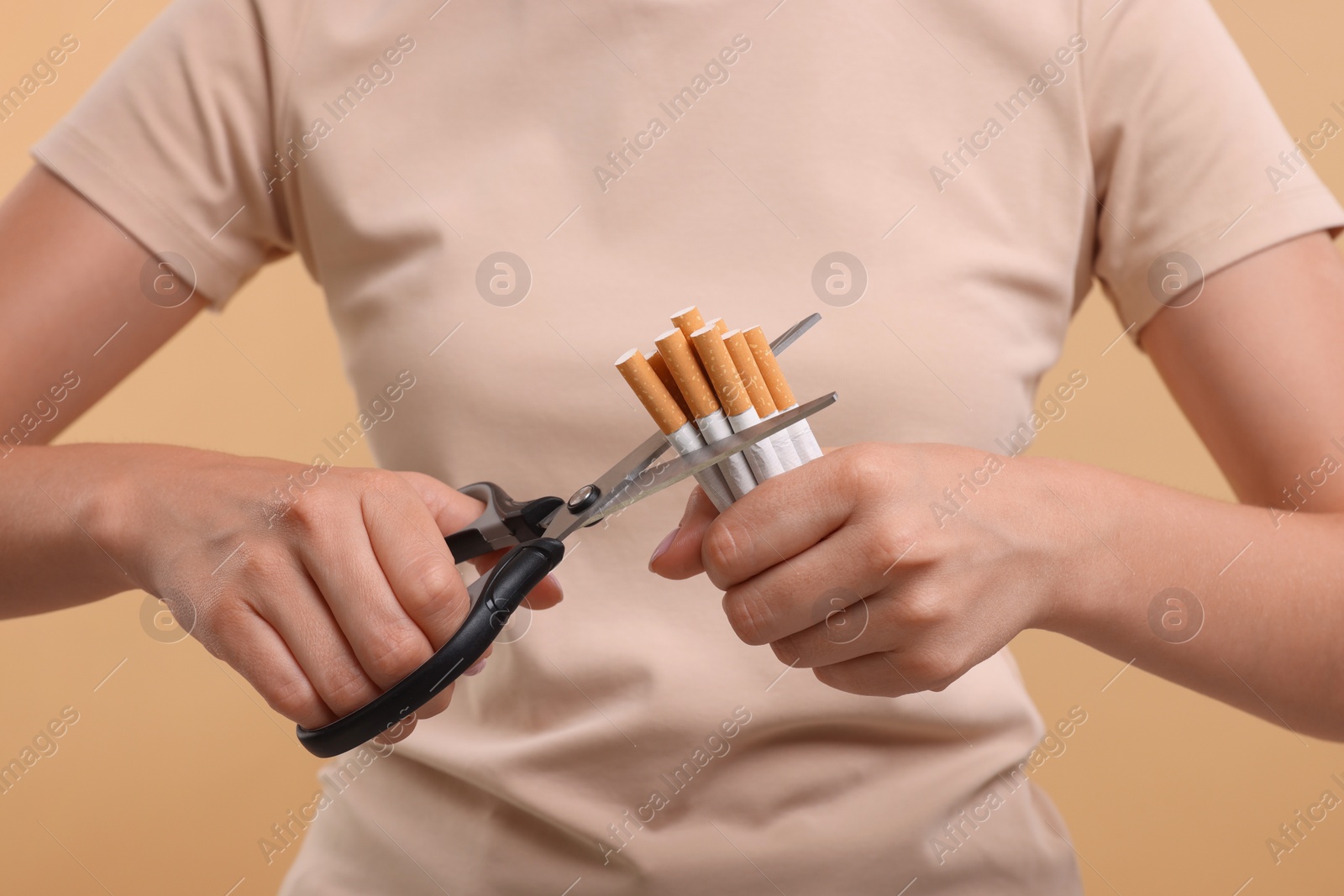 Photo of Stop smoking concept. Woman cutting cigarettes on light brown background, closeup
