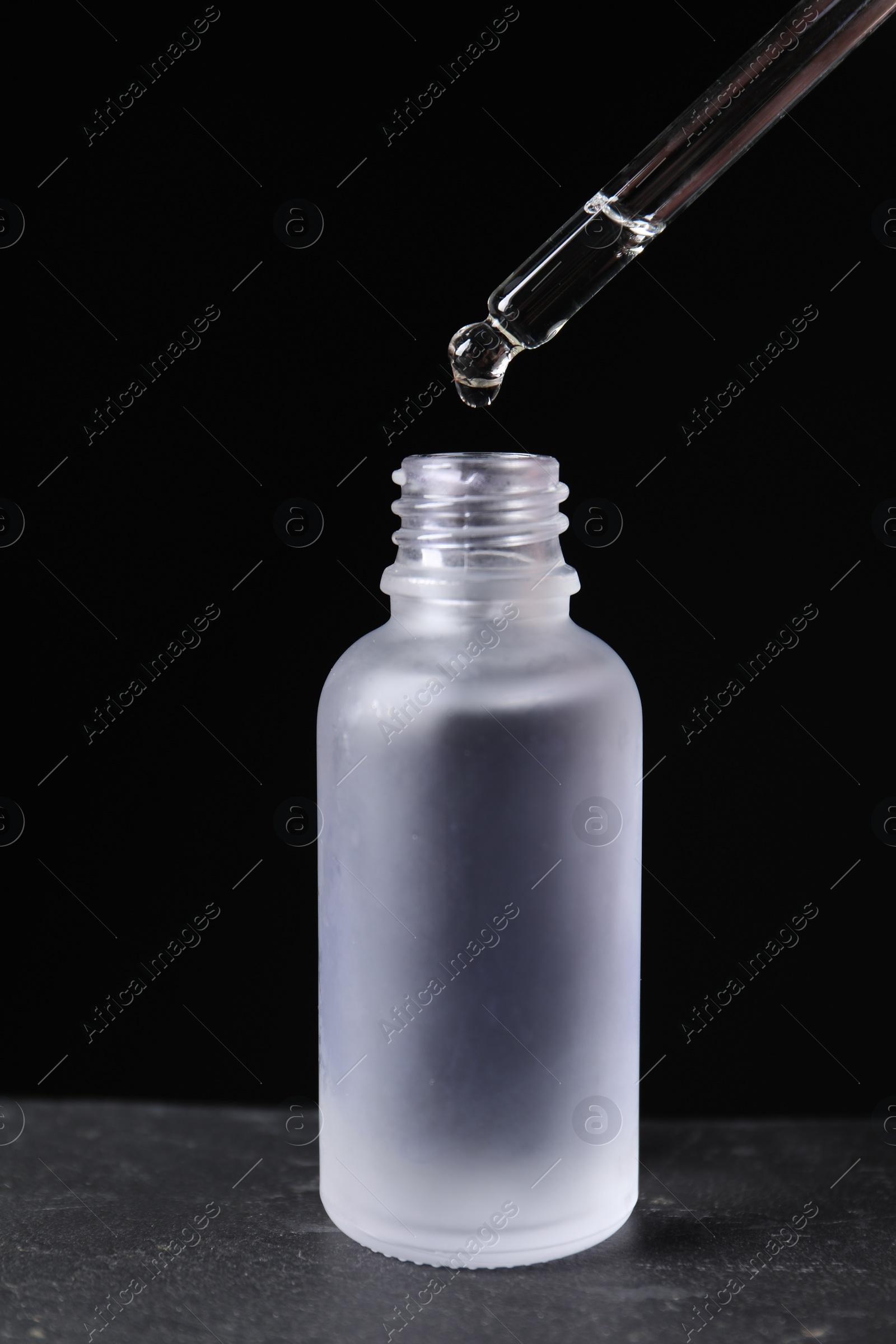 Photo of Dripping cosmetic serum from pipette into bottle on grey table
