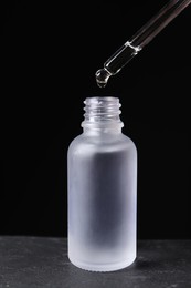 Dripping cosmetic serum from pipette into bottle on grey table