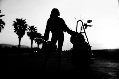 Image of Silhouette of woman posing near motorcycle on road
