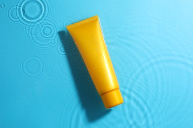 Photo of Tube with moisturizing cream in water on light blue background, top view