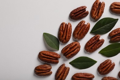Photo of Delicious pecan nuts and green leaves on white background, flat lay. Space for text