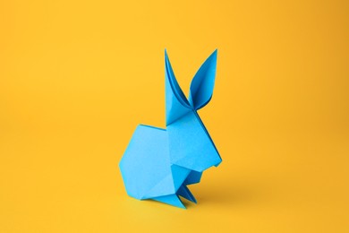 Origami art. Handmade light blue paper bunny on yellow background, closeup