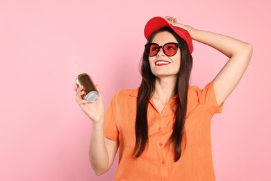 Beautiful young woman holding tin can with beverage on pink background