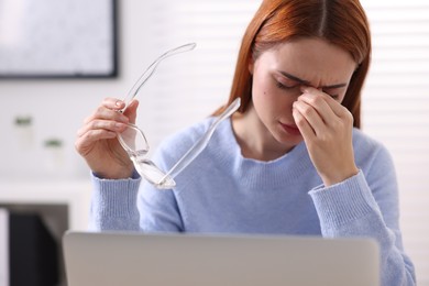 Woman with glasses suffering from headache at workplace in office