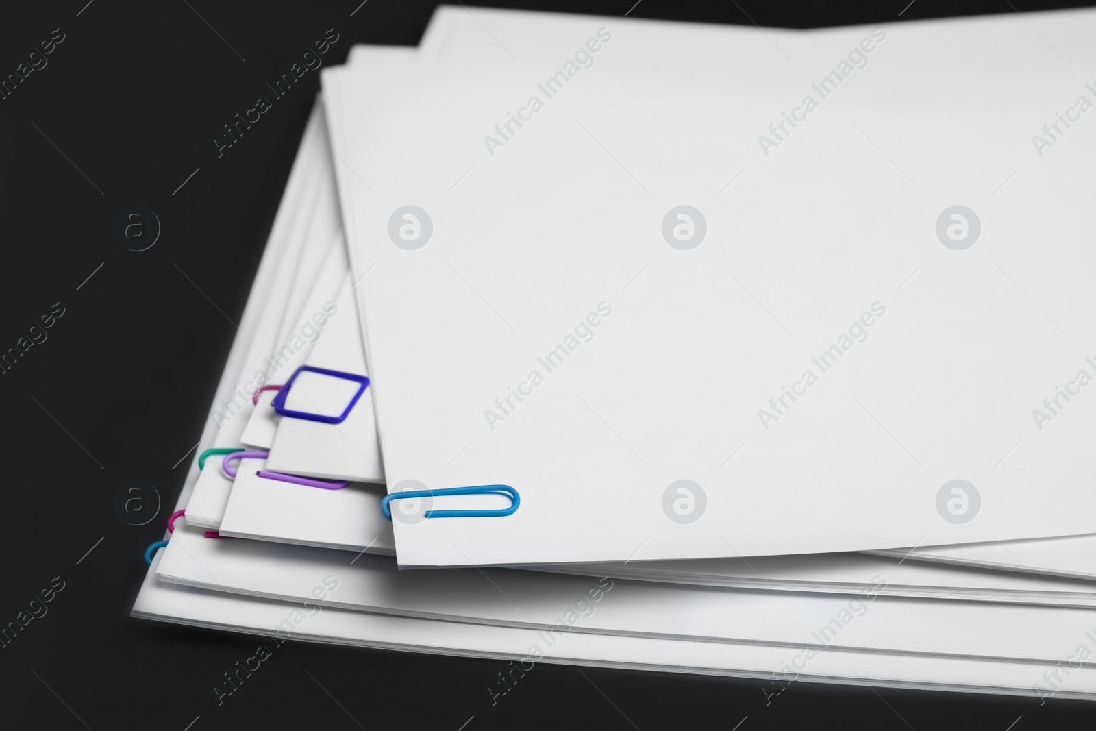 Photo of Sheets of paper with clips on black background, closeup