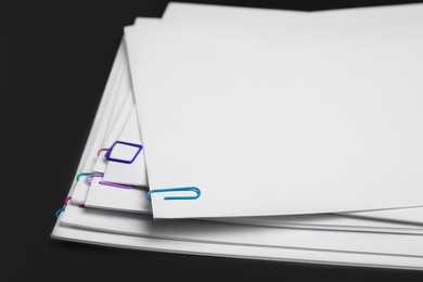 Photo of Sheets of paper with clips on black background, closeup