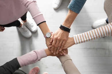 Photo of People holding hands together over light wooden background, top view. Unity concept
