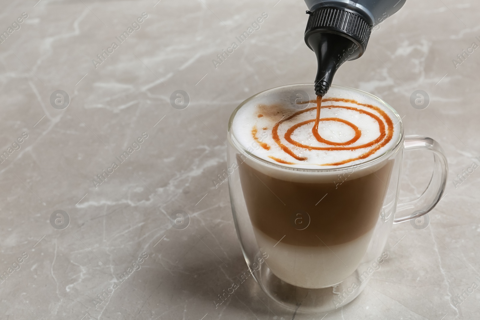 Photo of Adding caramel topping to latte macchiato on table, space for text