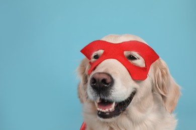 Adorable dog in red superhero mask on light blue background, space for text