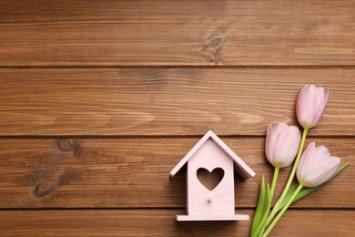 Photo of Beautiful bird house with heart shaped hole and tulips on wooden background, space for text. Spring flat lay composition