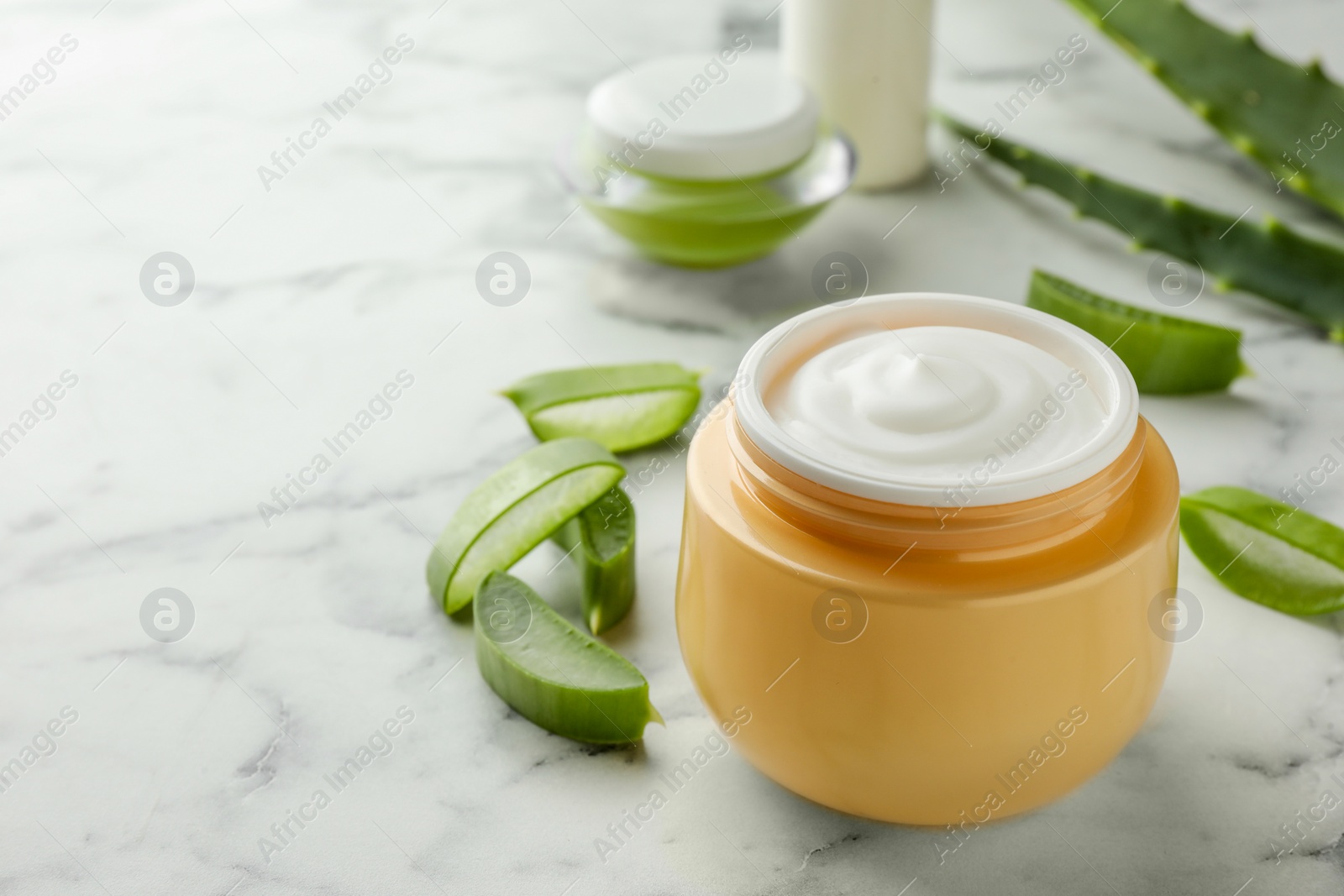 Photo of Jar with cream and cut aloe leaves on white marble table, closeup. Space for text