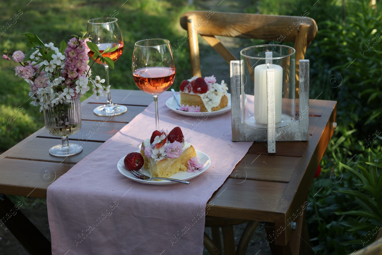 Photo of Vase with spring flowers, wine and cake on table served for romantic date in garden