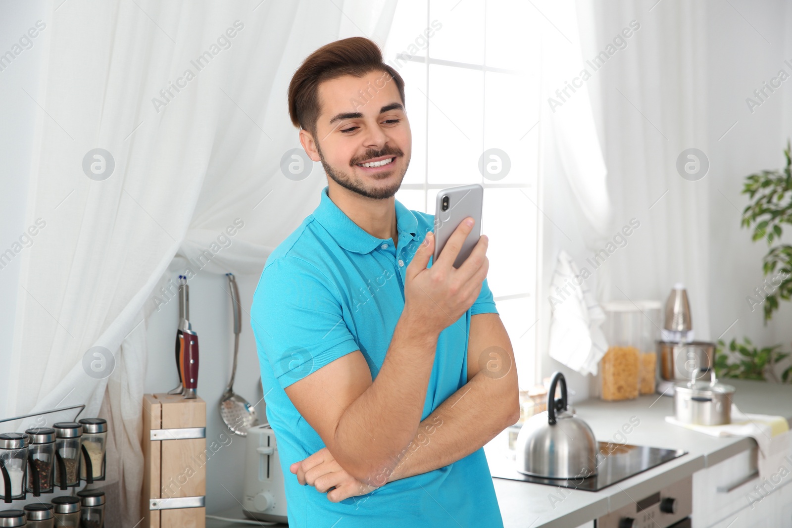 Photo of Young man laughing while using smartphone in kitchen