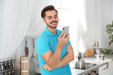 Young man laughing while using smartphone in kitchen