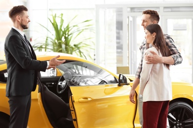 Photo of Young couple buying new car in salon