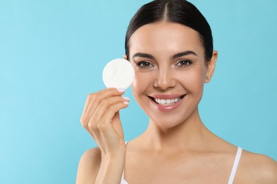 Photo of Young woman using cotton pad with micellar water on light blue background