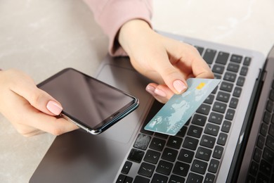Photo of Online payment. Woman using credit card and smartphone near laptop at light grey table, closeup
