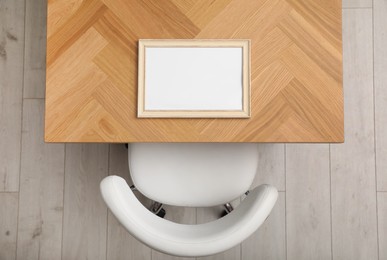 Photo of Empty photo frame on wooden table near chair indoors, top view