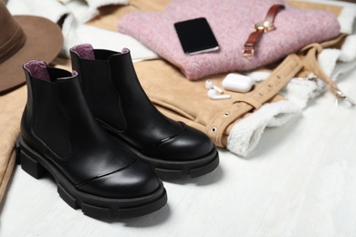 Black leather boots, clothes and accessories on white wooden background
