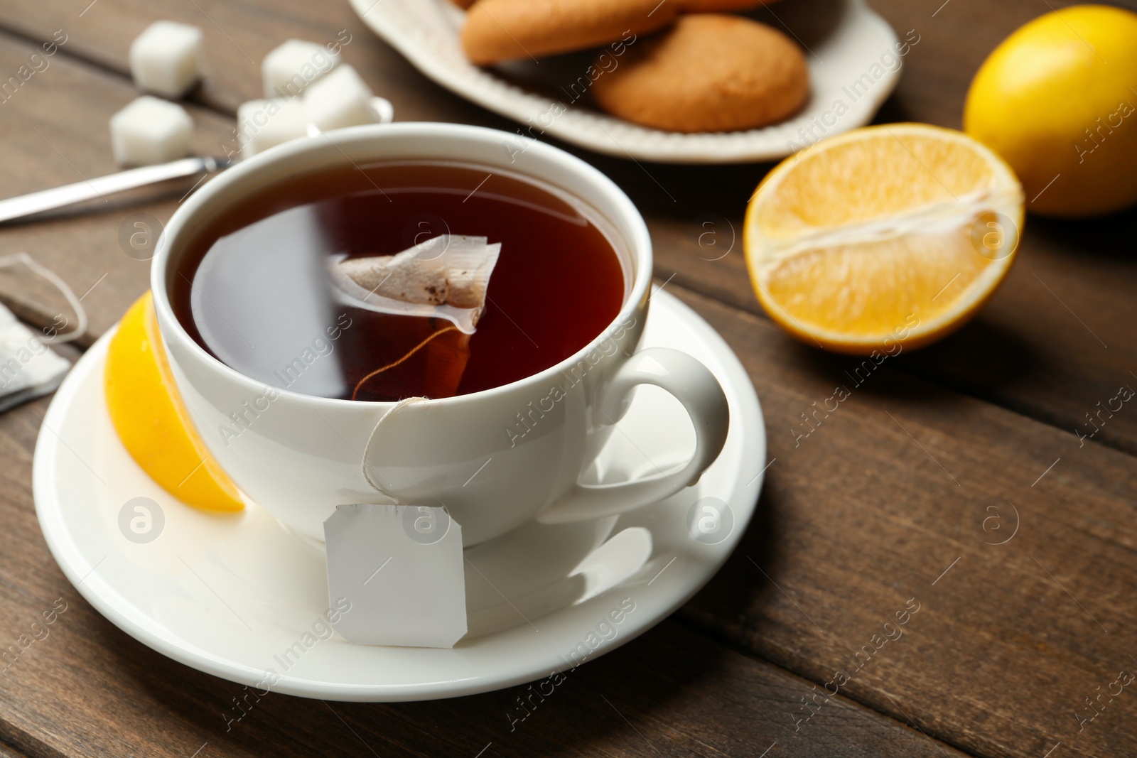 Photo of Tea bag in ceramic cup of hot water and lemon on wooden table