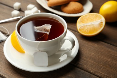 Photo of Tea bag in ceramic cup of hot water and lemon on wooden table