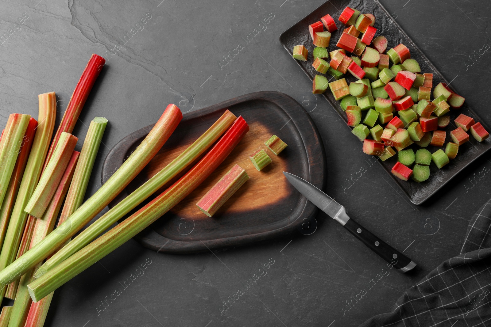 Photo of Whole and cut rhubarb stalks and knife on black table, flat lay