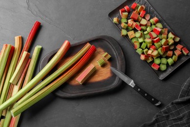 Photo of Whole and cut rhubarb stalks and knife on black table, flat lay