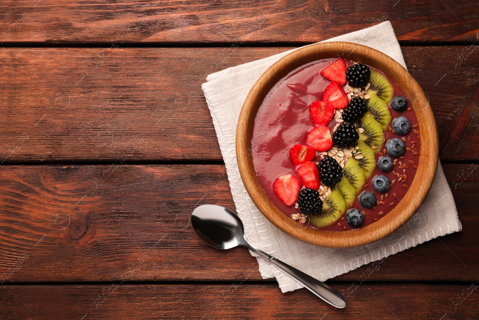 Photo of Bowl of delicious smoothie with fresh blueberries, strawberries, kiwi slices and blackberries on wooden table, flat lay. Space for text