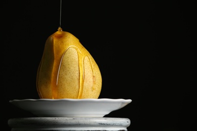 Photo of Pouring sweet syrup onto fresh ripe pear on plate against dark background. Space for text