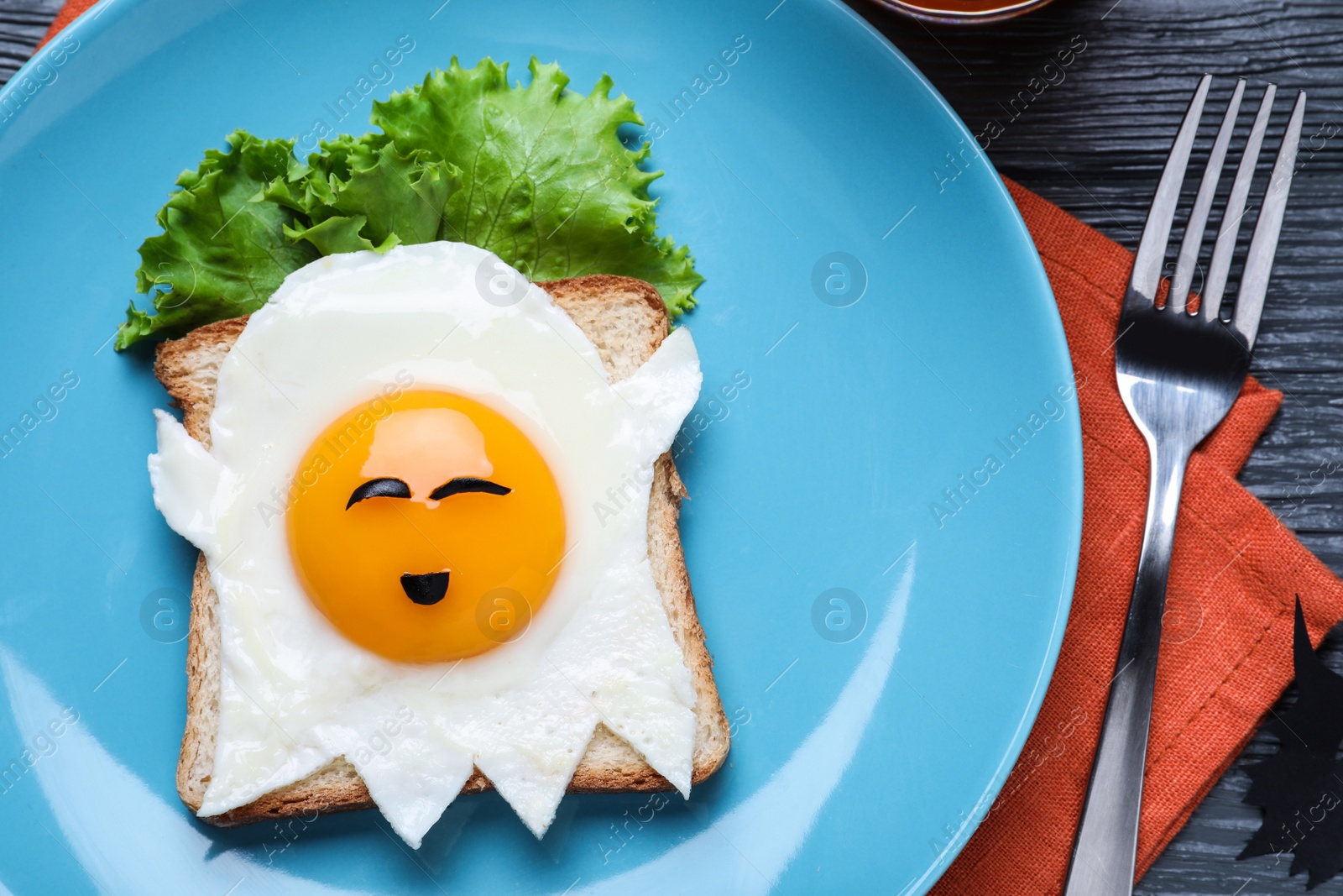 Photo of Halloween themed breakfast served on black wooden table, flat lay. Tasty toast with fried egg in shape of ghost