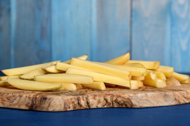 Photo of Cut raw potatoes on blue wooden table, closeup. Cooking delicious French fries