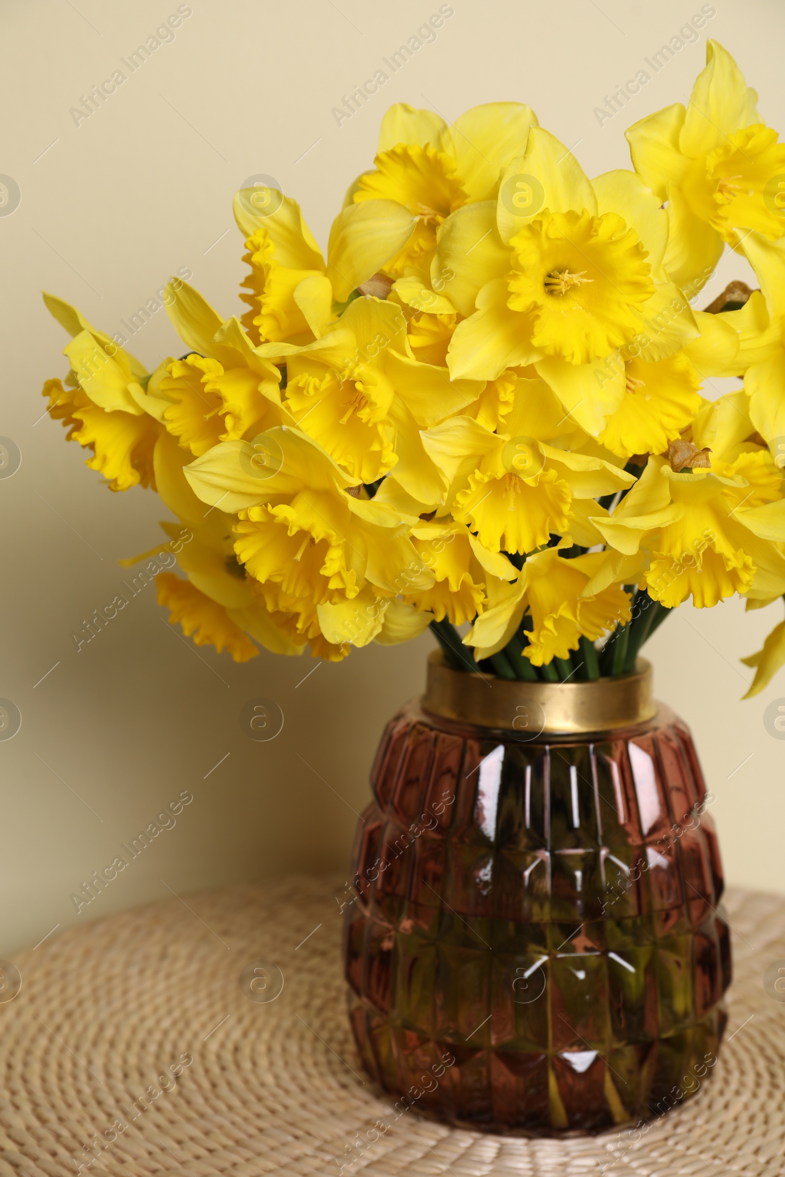 Photo of Beautiful daffodils in vase on wicker table near light wall
